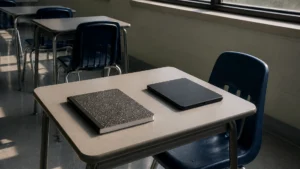 An empty classroom desk with a closed notebook and a tablet face-down.